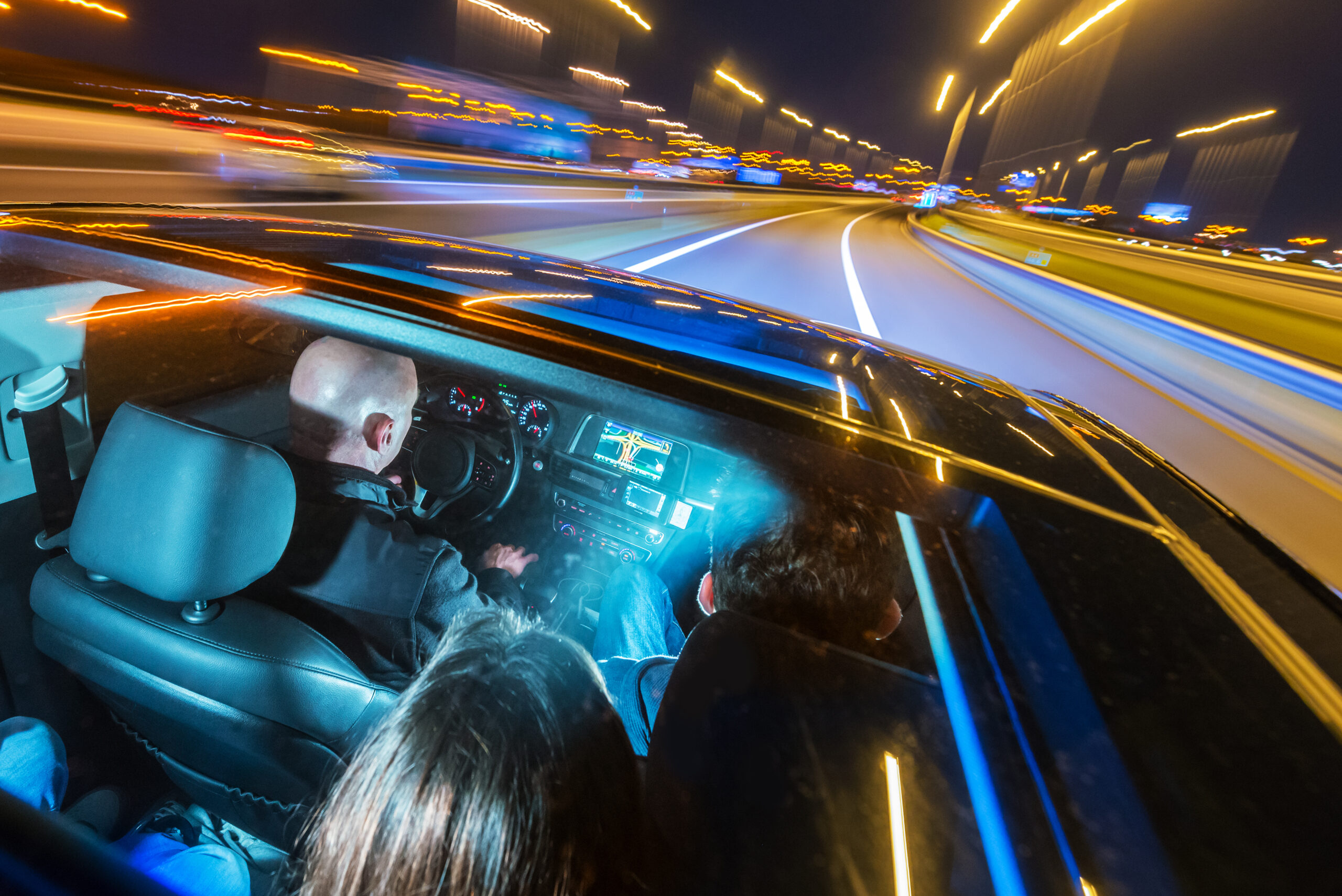 Car pooling and mobility concept, shown by a full passengers car sharing a ride, seen from the roof, through the sun roof at night, entering a motorway.